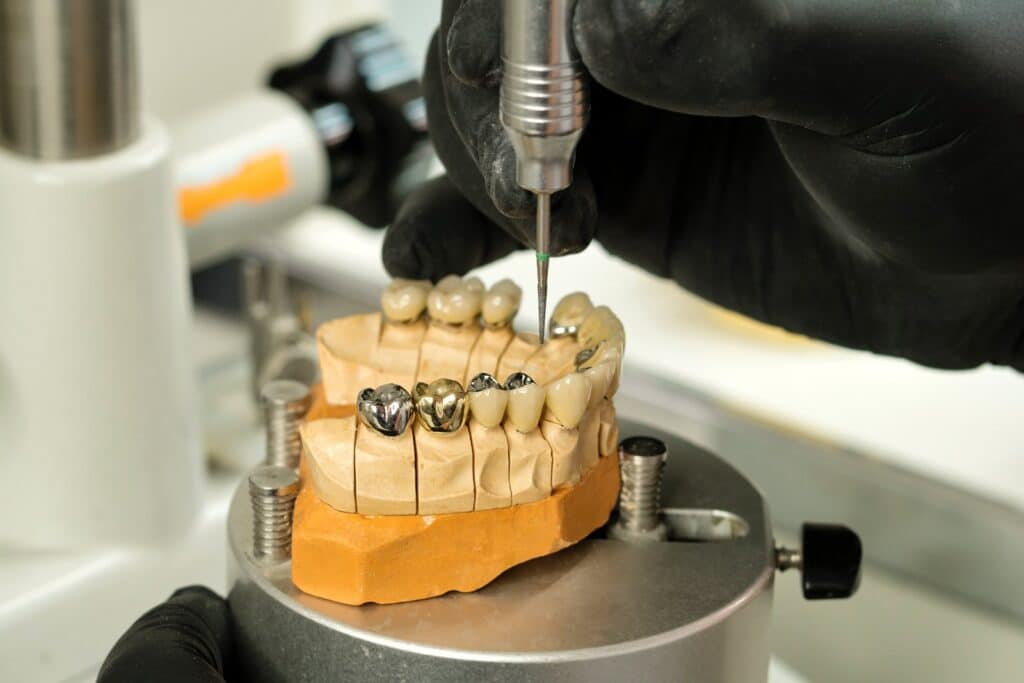 A dental technician working on a metal-framed dental model at a laboratory bench.