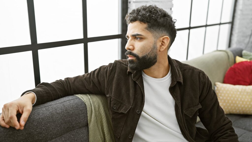 Relaxed man seated beside a large window in a bright, modern room