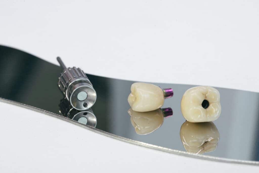Two zirconium crowns on titanium abutments resting on a dental instrument.