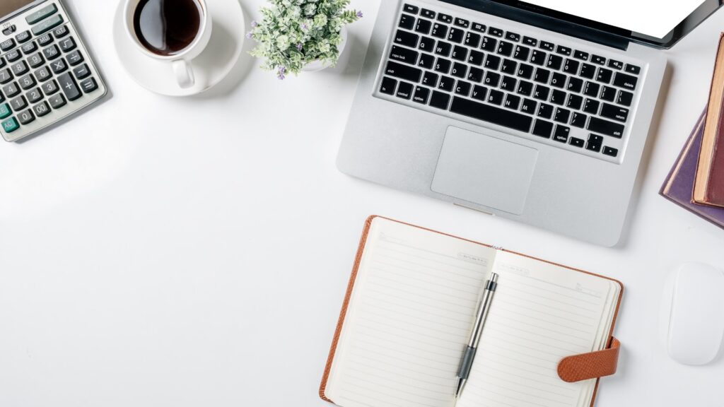 A calculator, an open notebook with a pen, a laptop and a cup of coffee on a white desk, illustrating a guide to what a gastric balloon costs in the UK and in Turkey